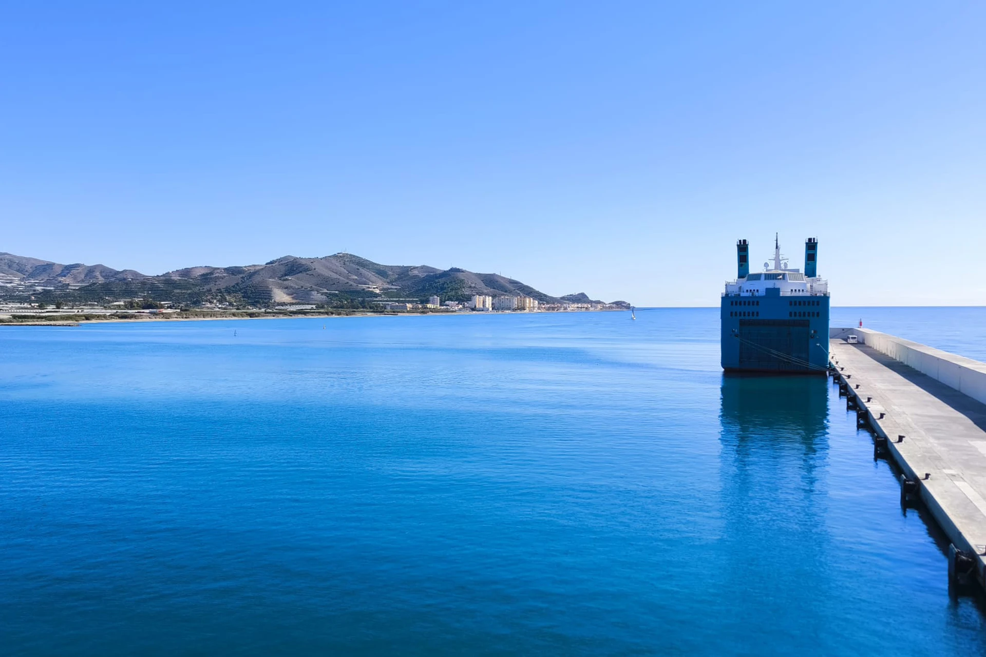 Imagen panorámica del puerto de Motril en un día soleado con cielo y aguas azules en la que aparece un crucero atracado en el muelle
